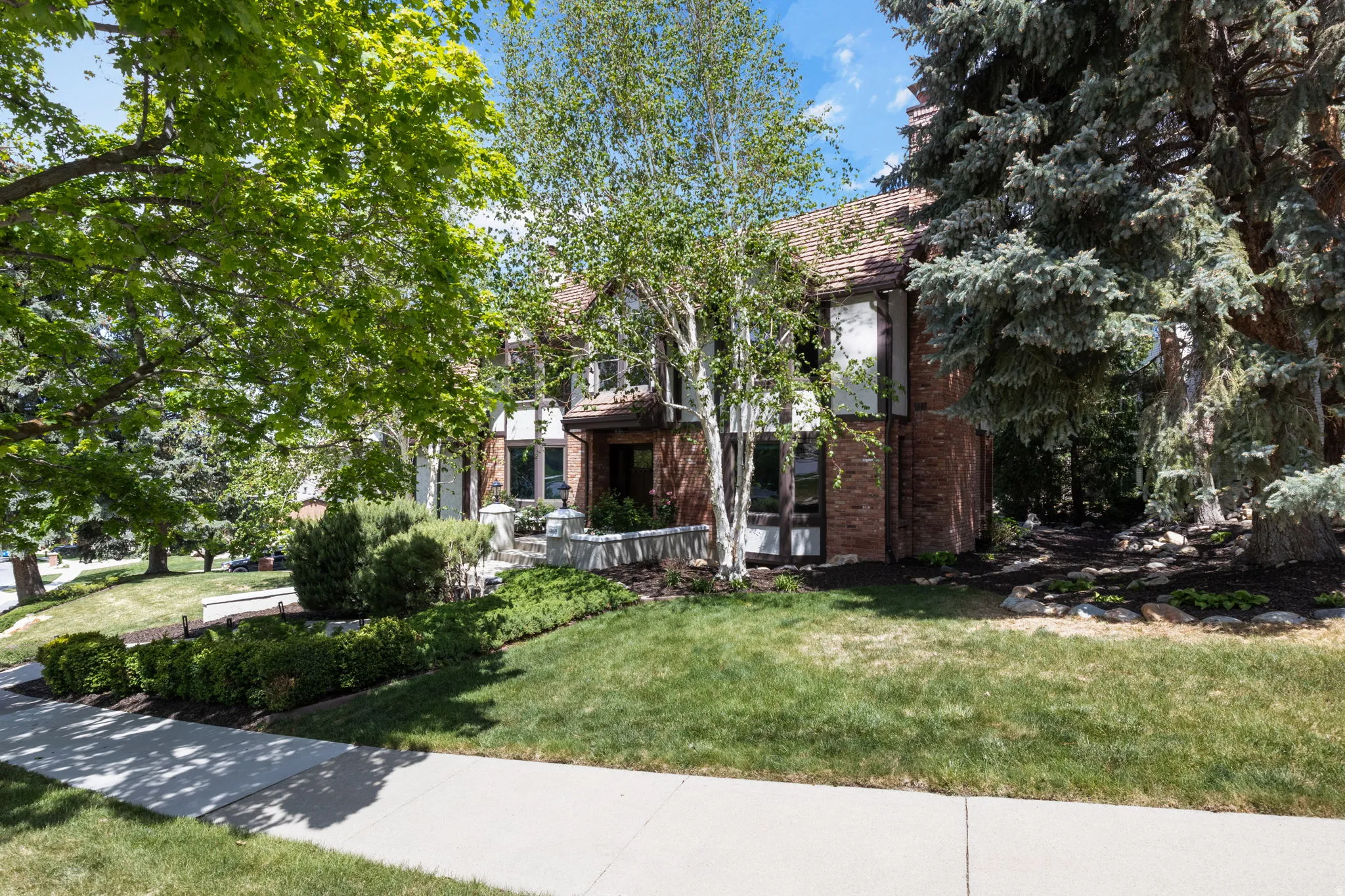 Brick exterior residence with a tiled roof, surrounded by mature trees and manicured landscaping