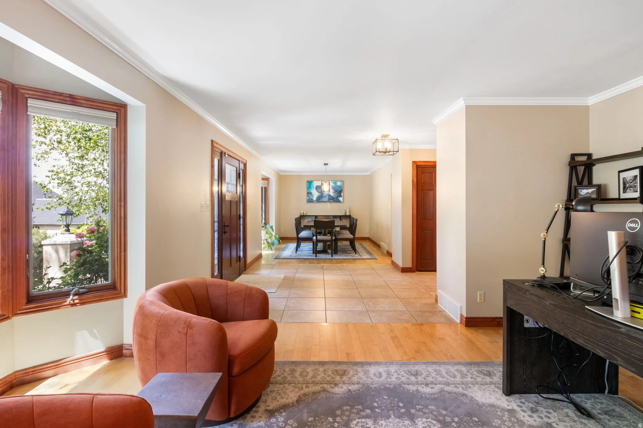 Spacious interior featuring a large bay window with wood trim, crown molding, wood-finish flooring, and natural stone-look tile