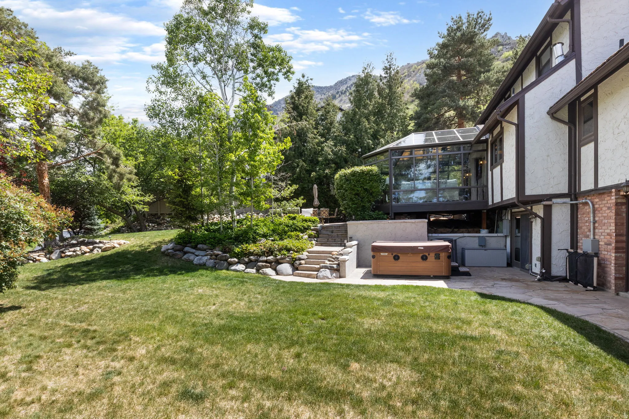 Expansive outdoor area featuring a spacious lawn, tiered landscaping with stone retaining walls, and mature trees