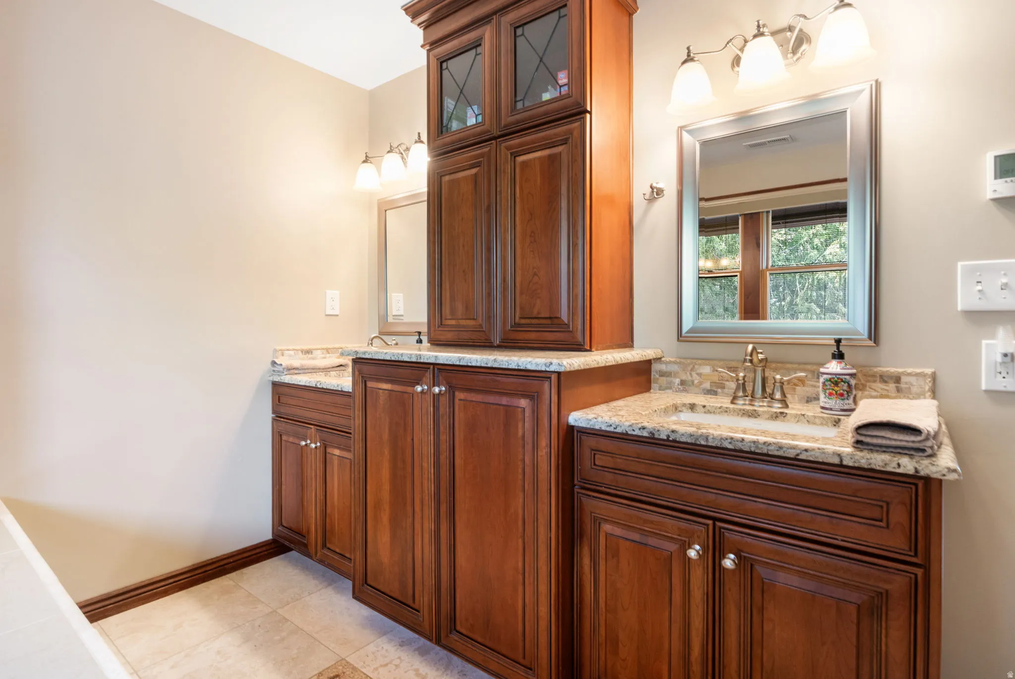 Primary Bathroom. vanity featuring dual sinks, granite countertops, wood cabinetry, tile flooring, and a mirrored upper storage cabinet
