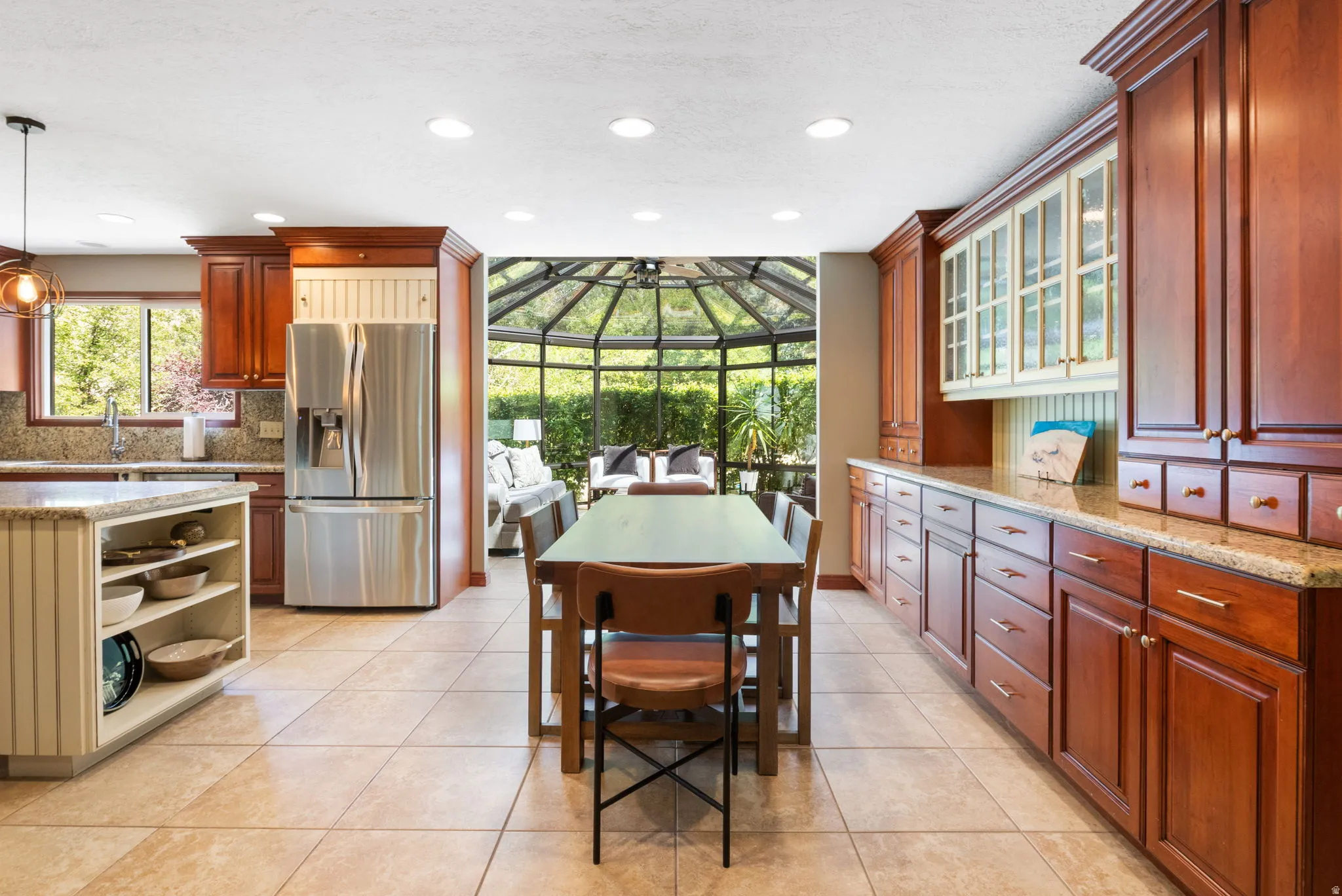 Kitchen featuring warm wood cabinetry, light-toned tile flooring, recessed ceiling lighting, a built-in stainless steel refrigerator, and granite countertops