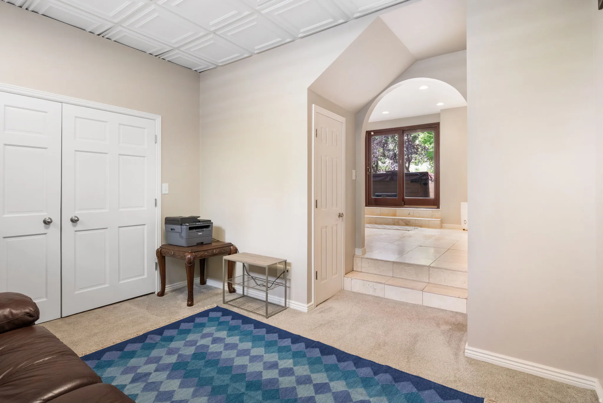 Recessed lighting illuminates an arched entryway leading to a tile-floored area with brown-framed sliding glass doors