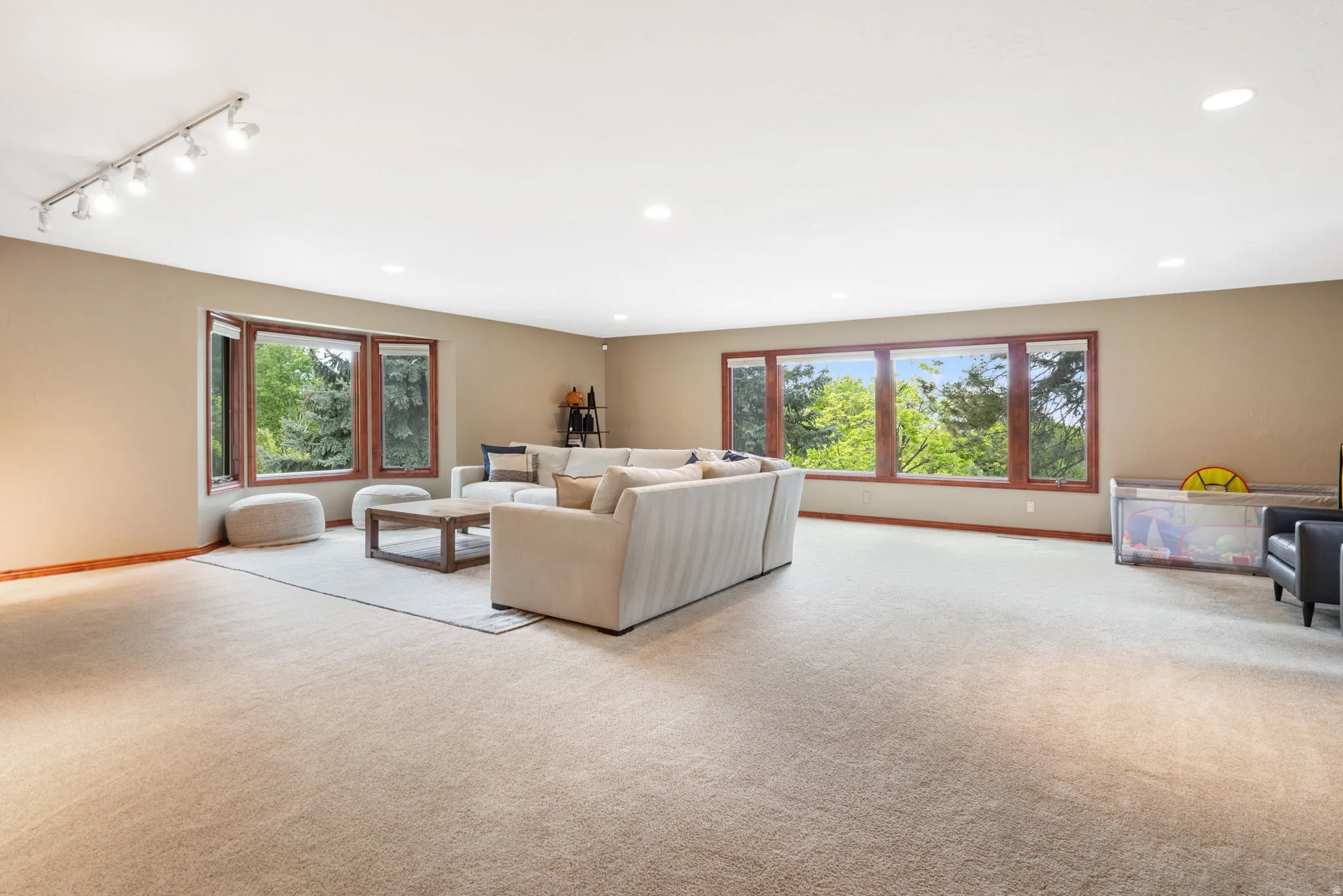 Spacious room featuring neutral carpeting, a large bay window, and a wall of additional windows with wood-finish trim