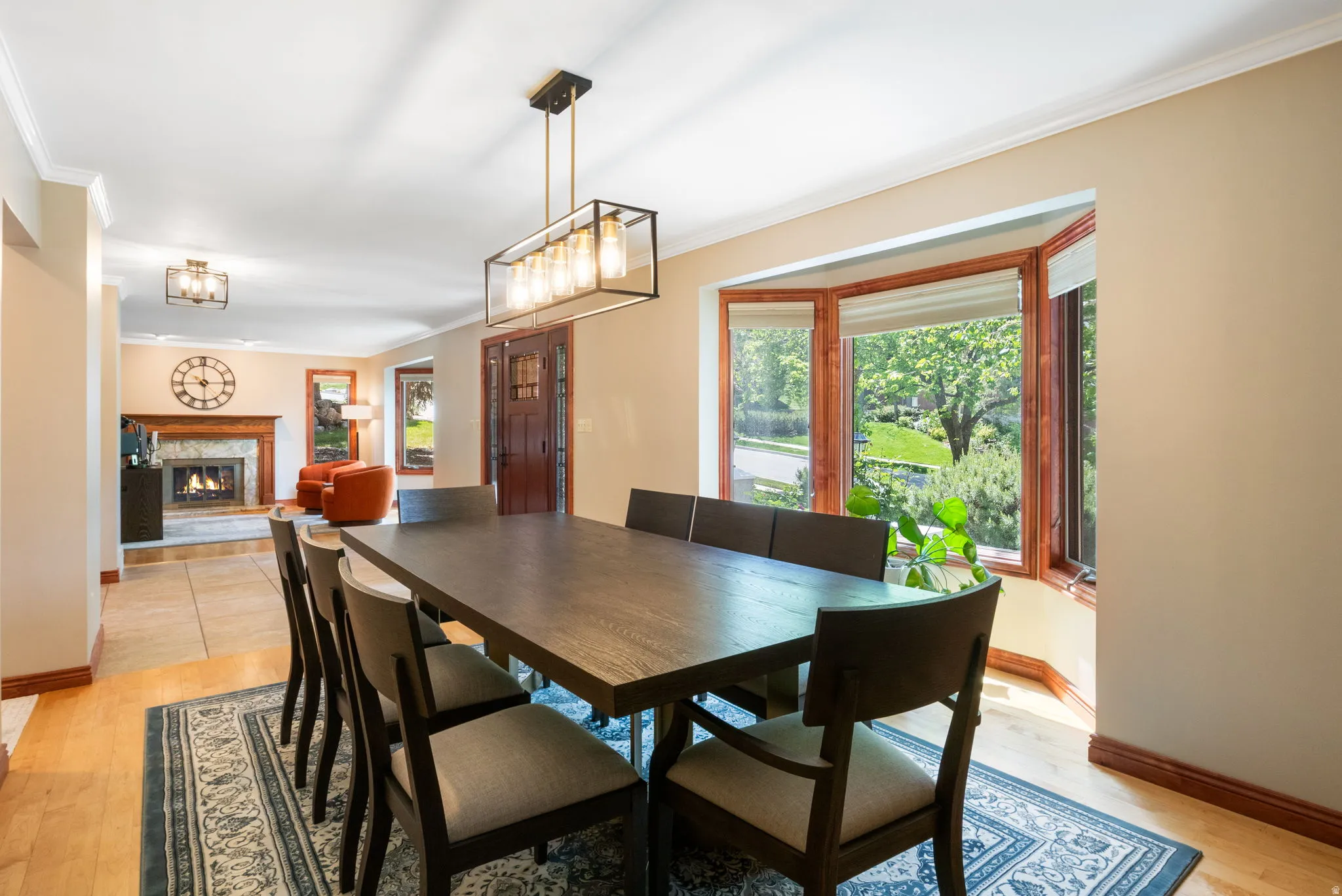 Dining area featuring wood-finish flooring, a rectangular chandelier with a dark metal frame, and a wide bay window with wood trim