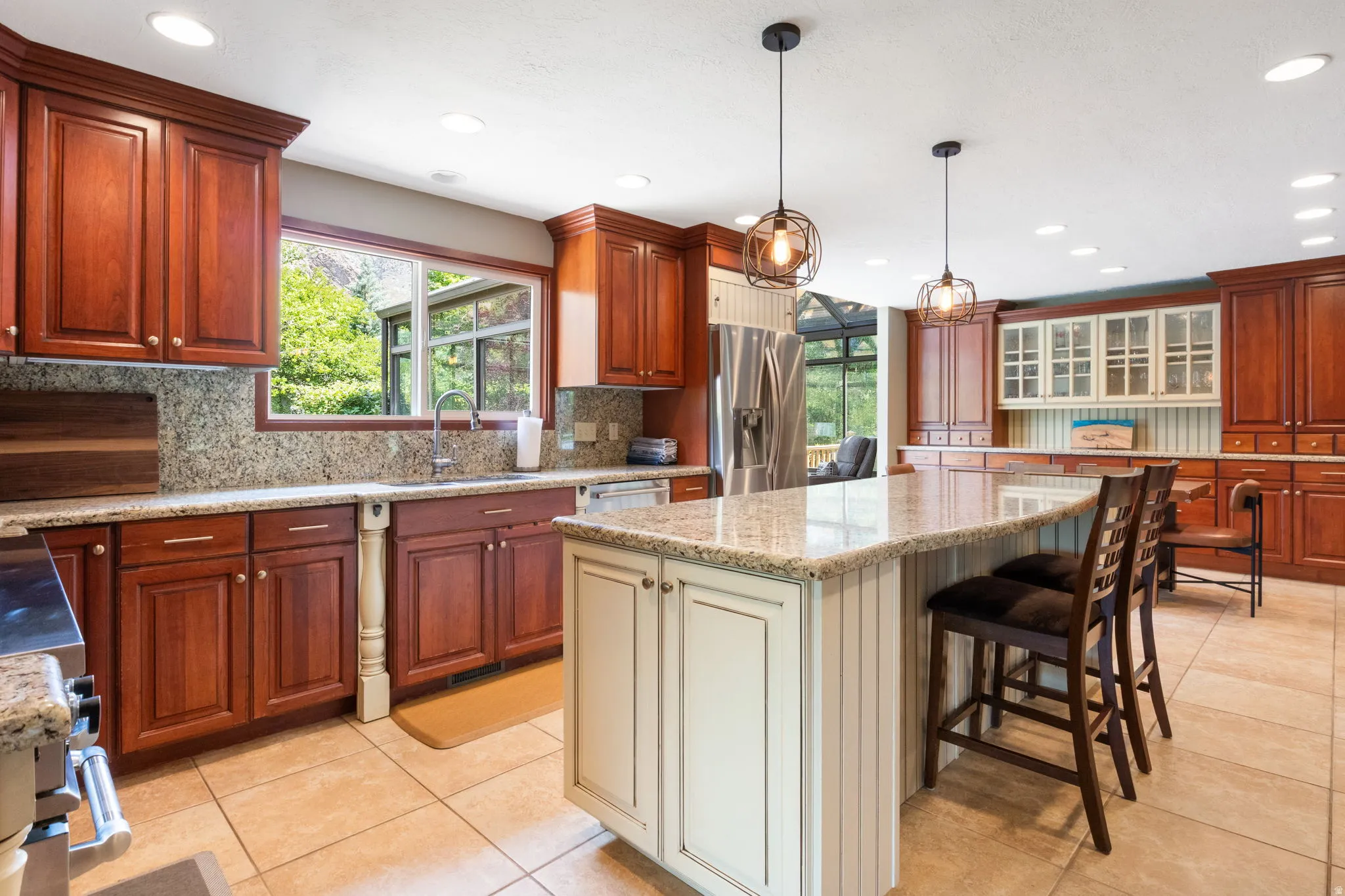 Expansive kitchen featuring a large central island with seating, granite countertops, tile flooring, rich wood cabinetry, and stainless steel appliances