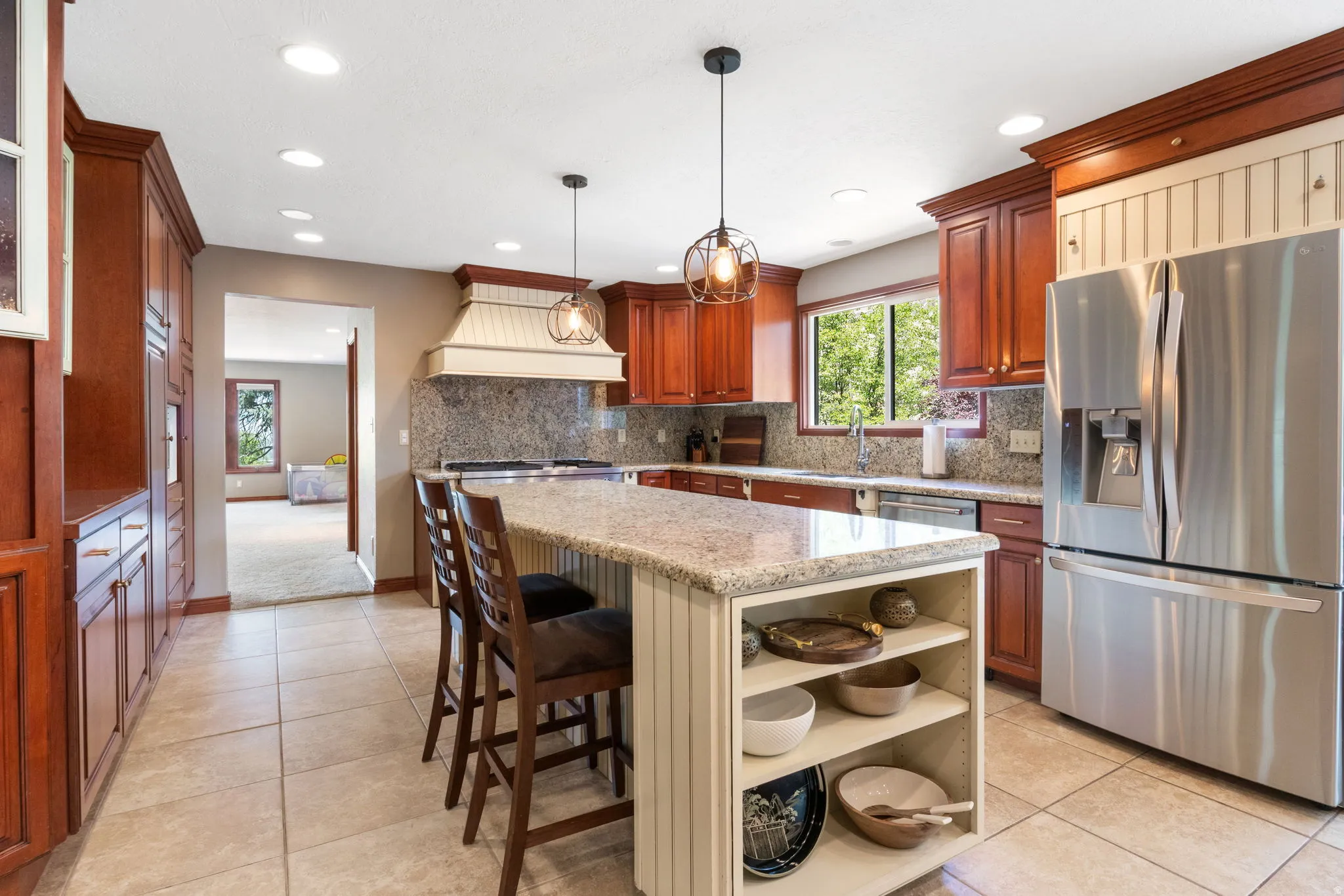 Kitchen featuring a central island with integrated shelving, granite countertops, tile flooring, rich wood cabinetry, and stainless steel appliances