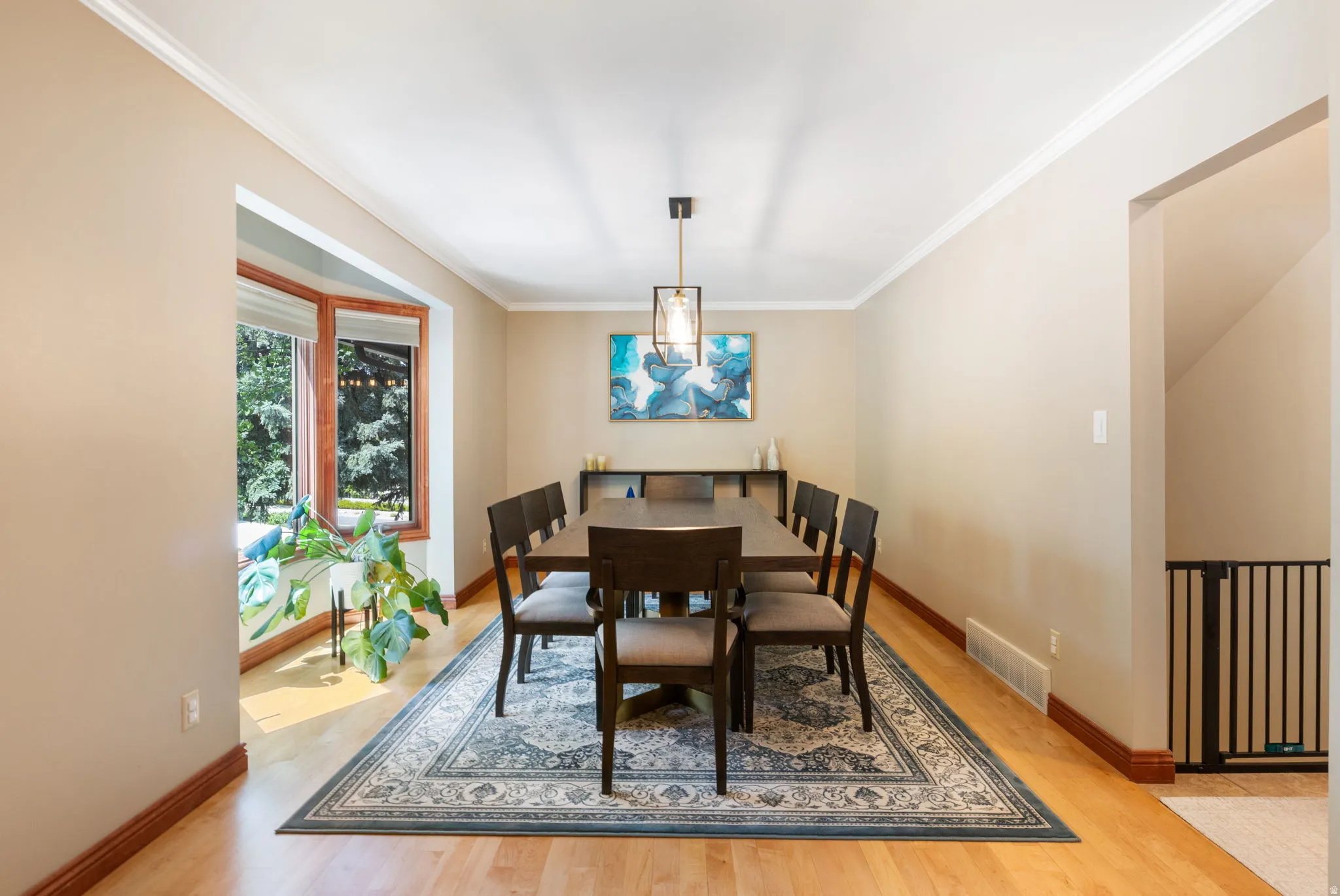 Dining space featuring wood-finish flooring, a bay window with wood trim, crown molding, and a contemporary pendant light fixture