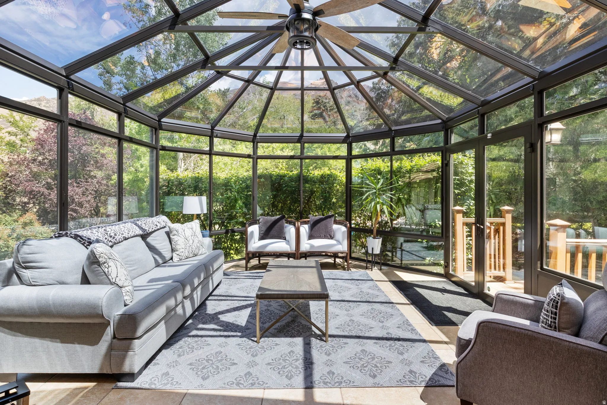 Expansive sunroom featuring a multi-faceted glass roof and walls, light-toned tile flooring, and a ceiling fan