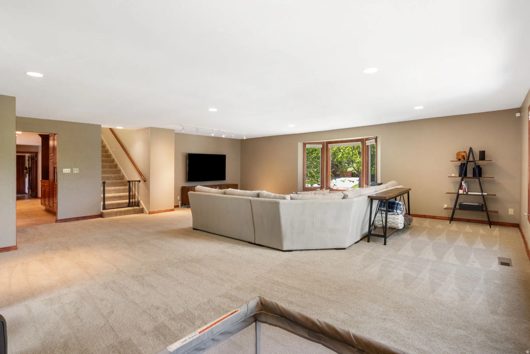 Spacious carpeted living area featuring recessed lighting, a bay window with wood-finish trim, a staircase with wood handrails and metal balusters, and an arched doorway
