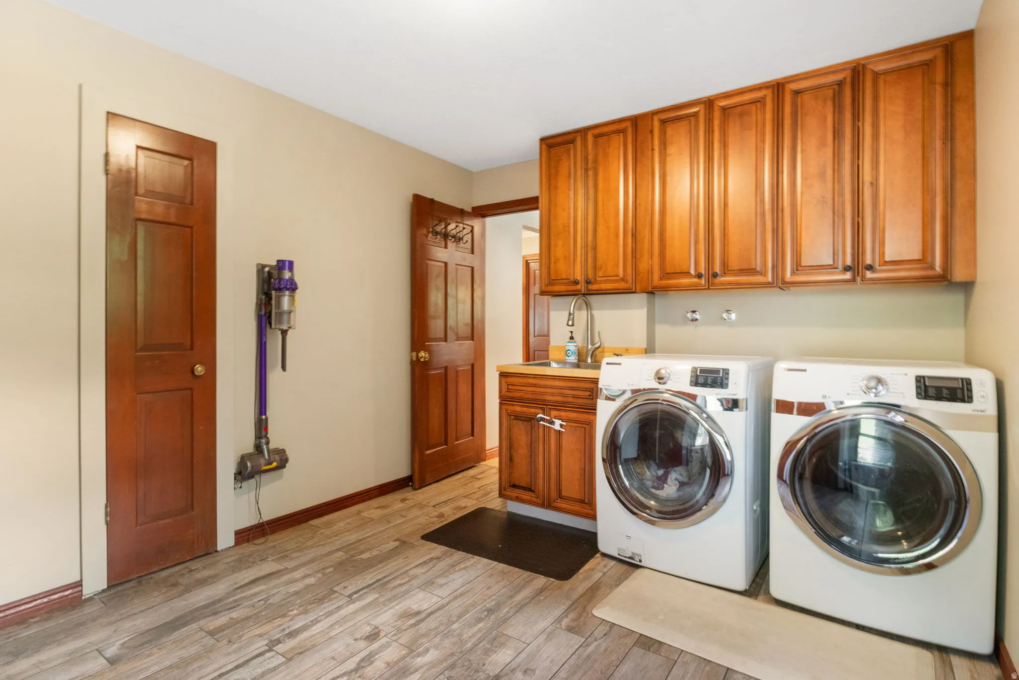 Laundry room featuring wood-finish flooring, built-in cabinetry, a utility sink with a chrome faucet, and a light neutral wall color