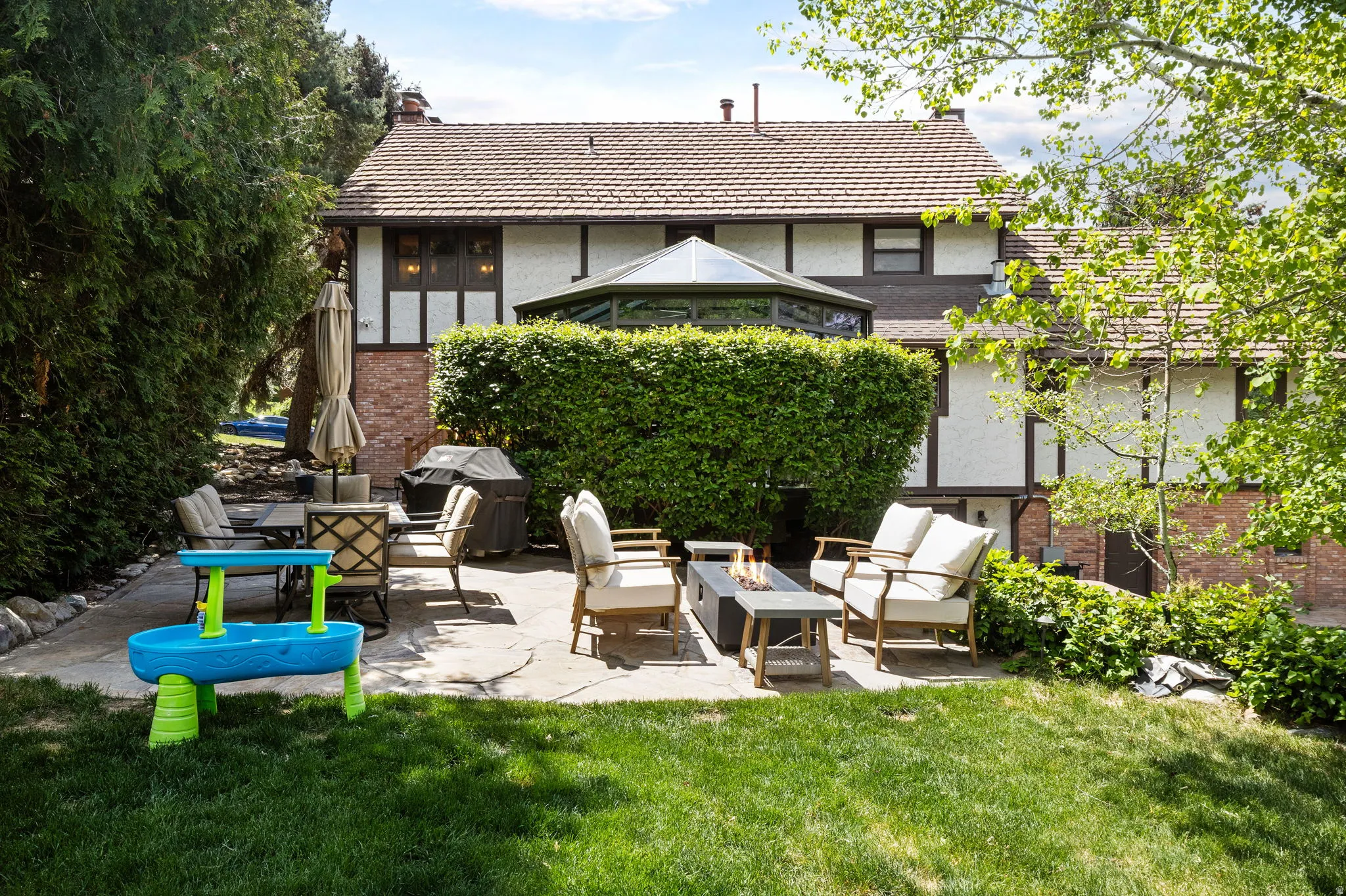 Expansive backyard featuring a stone patio, mature landscaping, and a substantial hedge