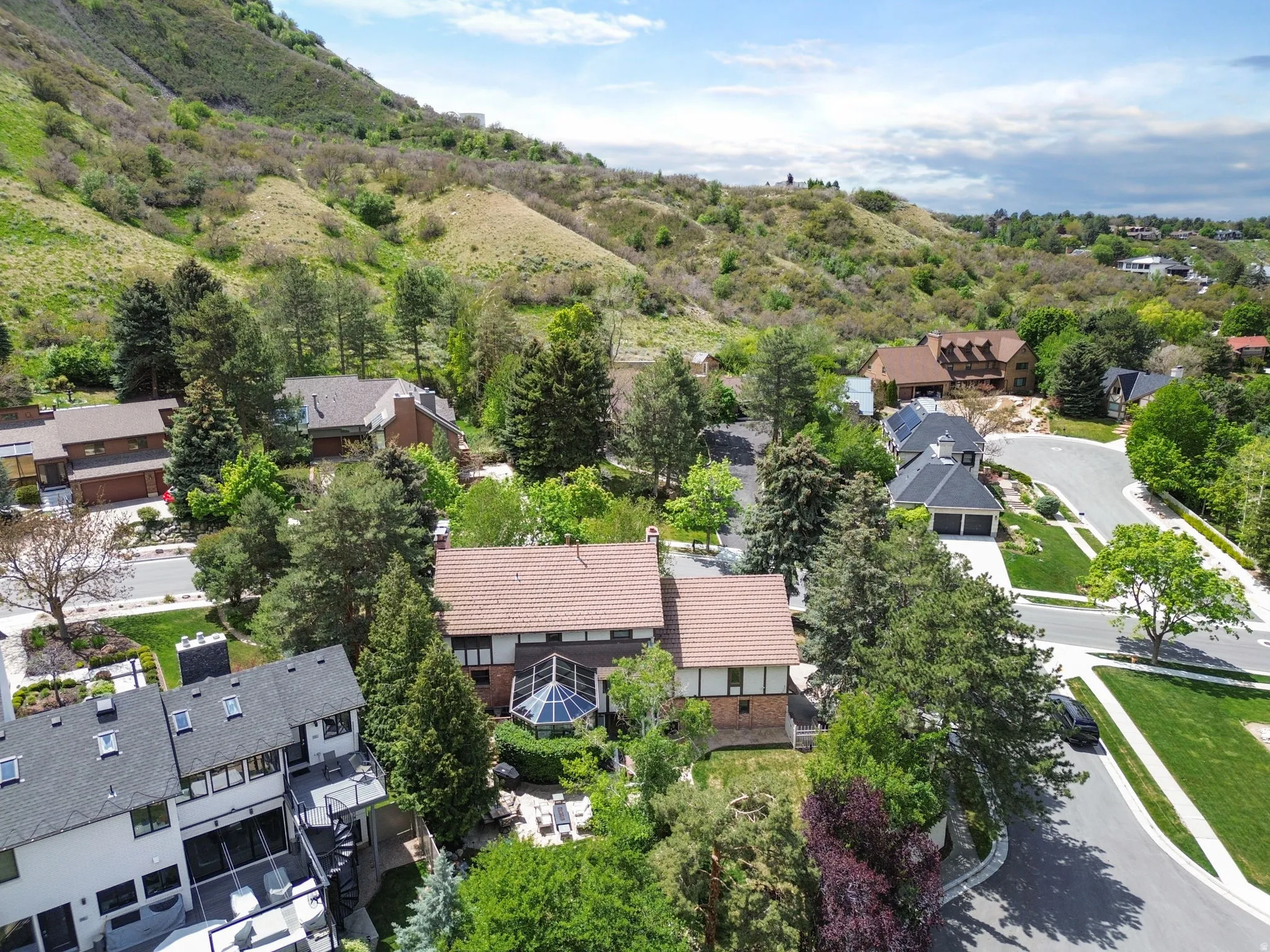 Aerial perspective showcasing a property with a distinct brown tile roof and an attached sunroom with a geometric glass enclosure