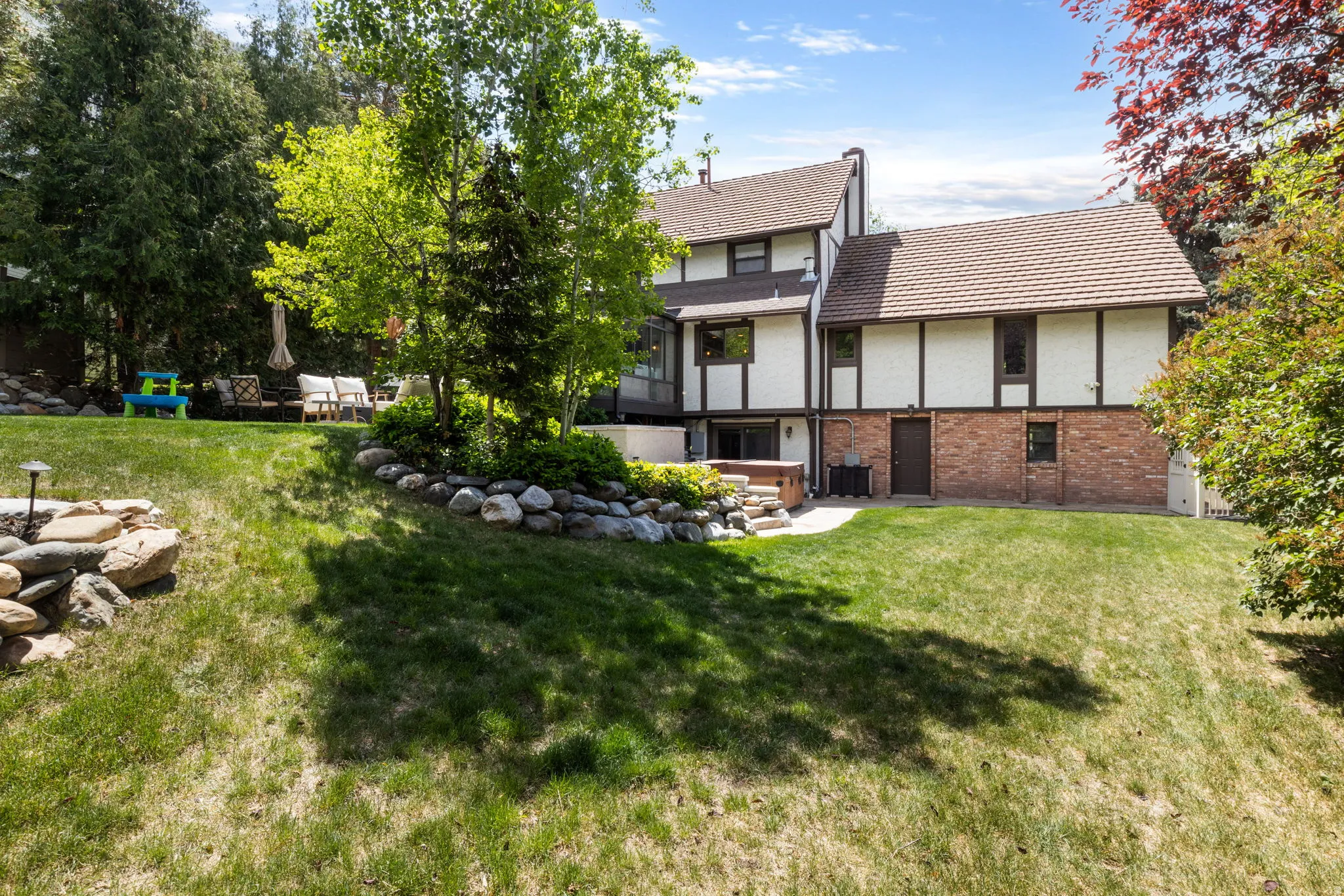 Expansive terraced backyard featuring a stone-lined garden bed, mature trees, and a paved patio area