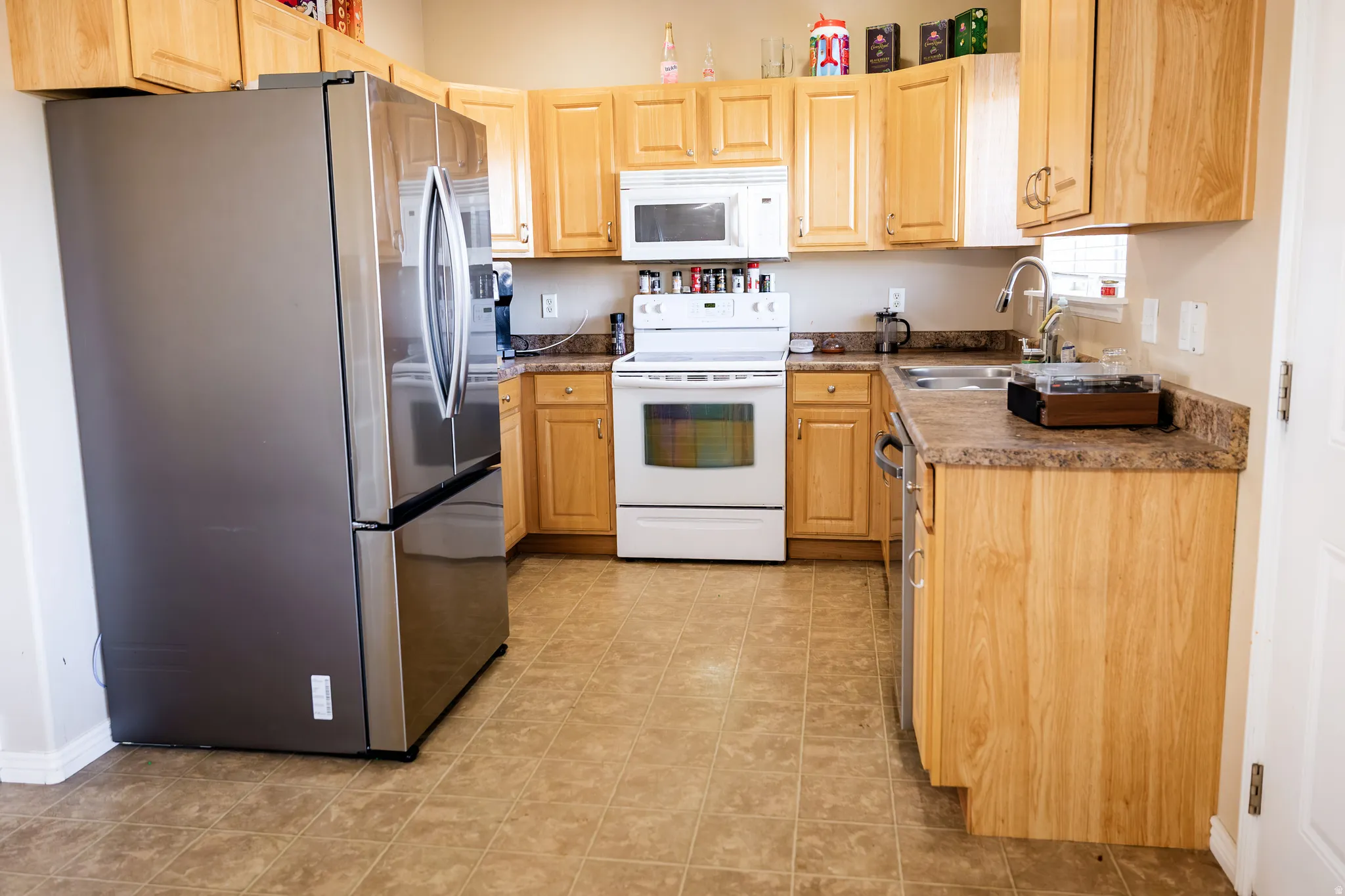 U-shaped kitchen featuring light wood cabinetry, laminate countertops, stainless steel refrigerator, white range, and white built-in microwave