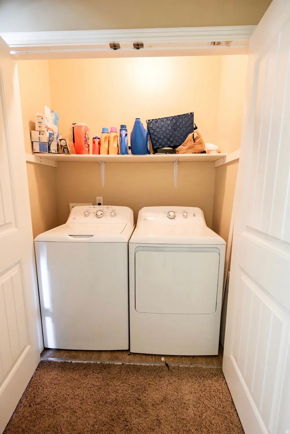 Dedicated laundry closet featuring a built-in shelf for storage, paneled bi-fold doors, and a neutral color palette
