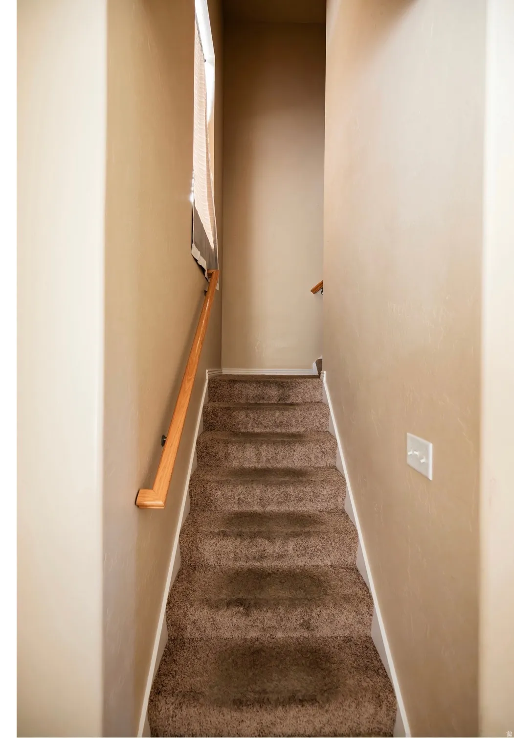Carpeted staircase with a wood handrail and neutral wall tones