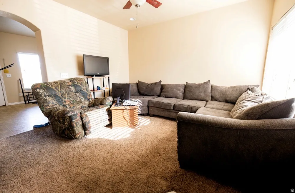 Carpeted living area featuring a ceiling fan, arched doorway, and light-toned walls