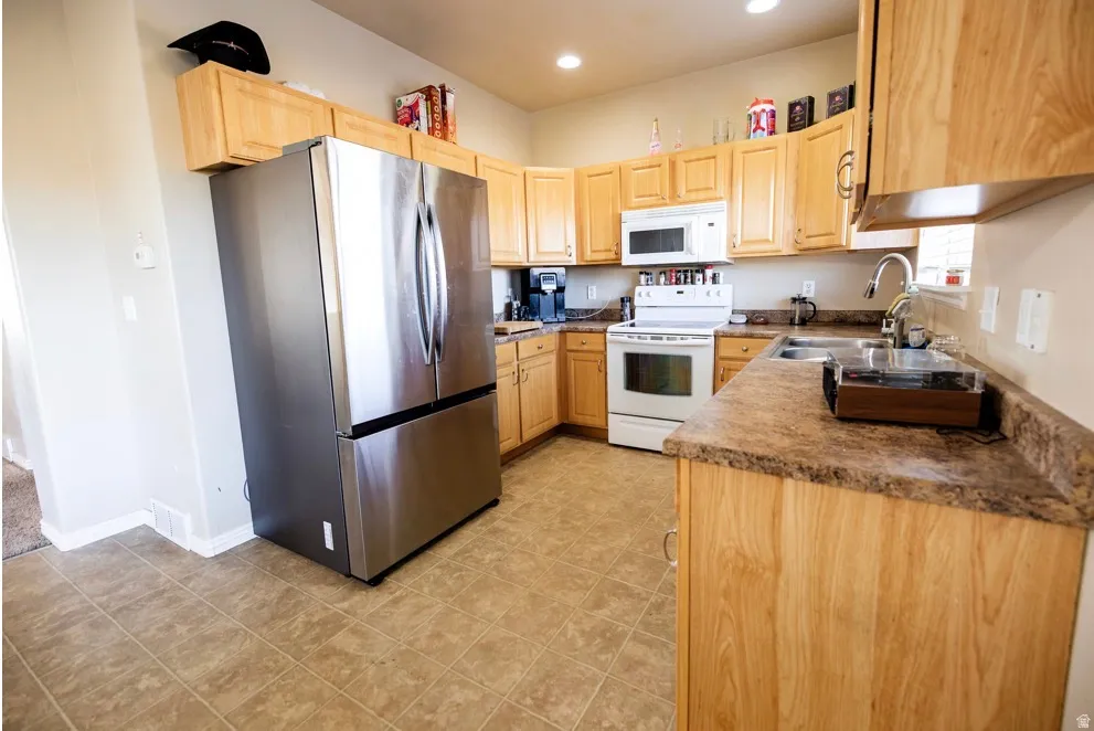 Kitchen featuring light wood cabinetry, a stainless steel refrigerator, white oven with an overhead microwave, and a double basin sink