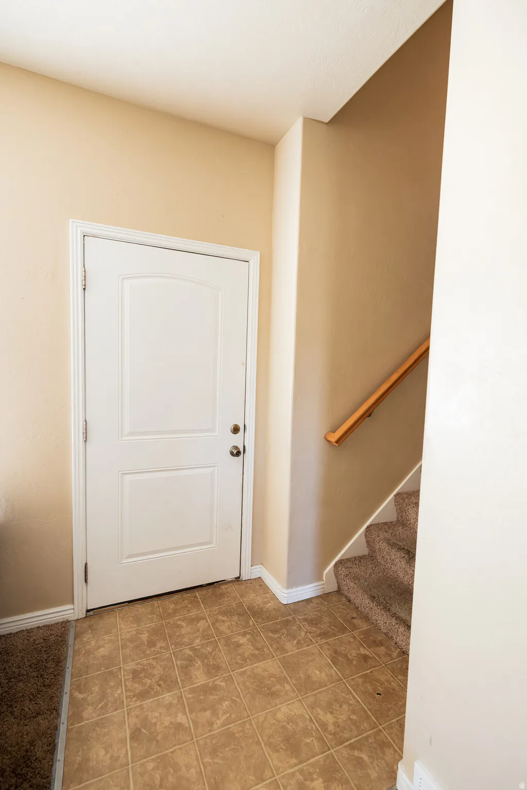Entryway featuring a white paneled door, square-tiled flooring, and a carpeted staircase with a wooden handrail