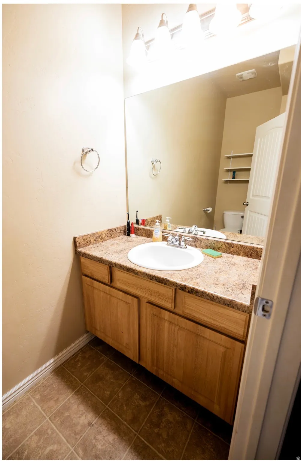 Bathroom vanity featuring a light wood-finish cabinet with a granite-look countertop and an undermount sink