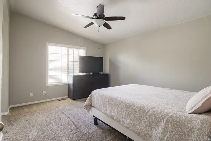 Bedroom featuring vaulted ceilings, a large window with blinds, carpet flooring, a ceiling fan with light, and neutral wall tones