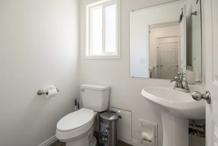 Bathroom featuring a pedestal sink with a chrome faucet, a rectangular mirror, and a window with white trim