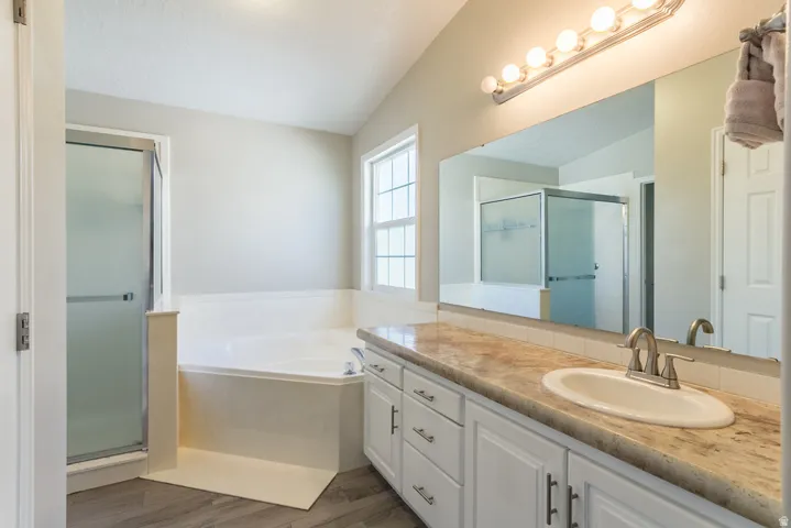 Bathroom featuring a built-in corner soaking tub, a separate glass-enclosed shower, and a single vanity with a solid surface countertop
