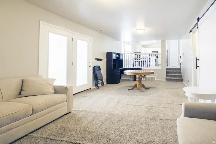 Carpeted recreation room featuring white French doors, a built-in entertainment center, a sliding barn door, and a staircase with coordinating carpet