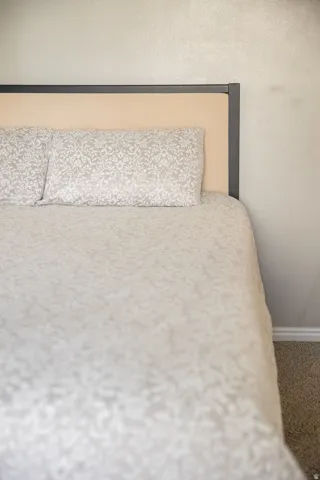 Bedroom featuring a modern headboard with a beige upholstered panel and dark frame, textured light-colored wall, and carpet flooring