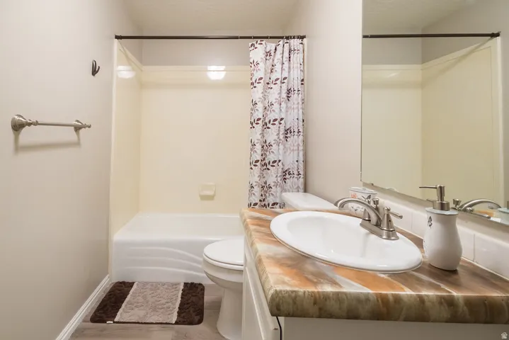 Bathroom featuring a white ceramic sink with a brushed nickel faucet, a spacious vanity with a multi-toned countertop, a full-width mirror, and a shower-over-tub combination