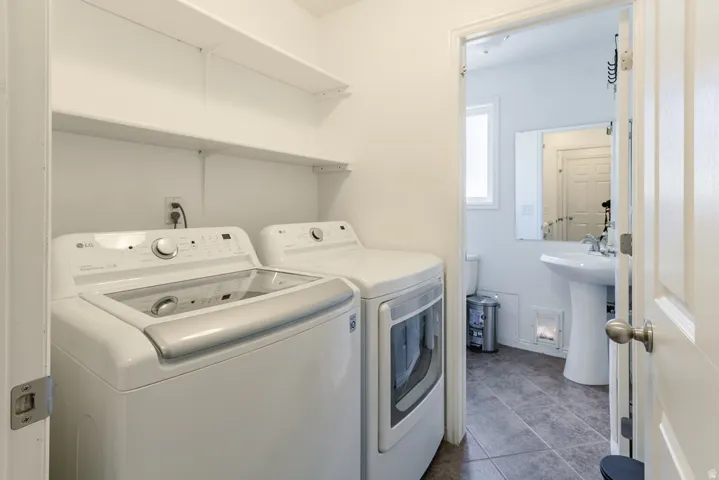Dedicated laundry area with built-in shelving and a partial view of a bathroom featuring a pedestal sink, wall-mounted mirror, and tile flooring