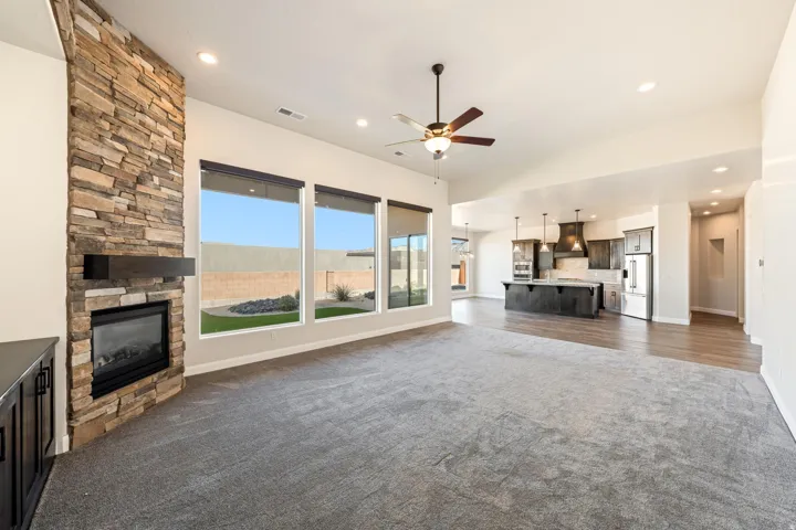 Spacious living area featuring a stacked stone fireplace with a dark wood mantel, large windows, a ceiling fan, and recessed lighting