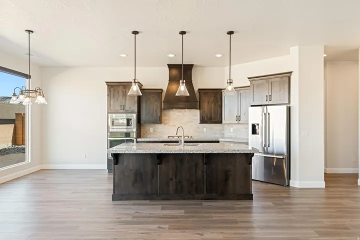 Open-concept kitchen featuring an oversized island with seating, stainless steel appliances, wood-finish flooring, recessed lighting, and a window with exterior views