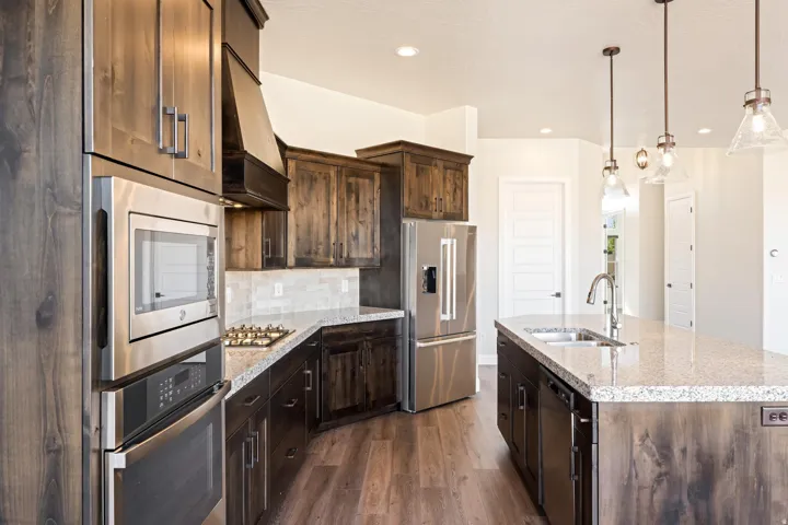 Spacious kitchen featuring dark wood-finish cabinetry, stainless steel appliances, light granite countertops, and wood-finish flooring