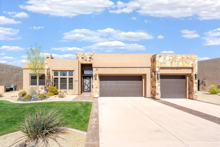 Southwestern-style exterior featuring a stone facade, stucco finishes, an enclosed entry, dual garage doors, and a concrete driveway