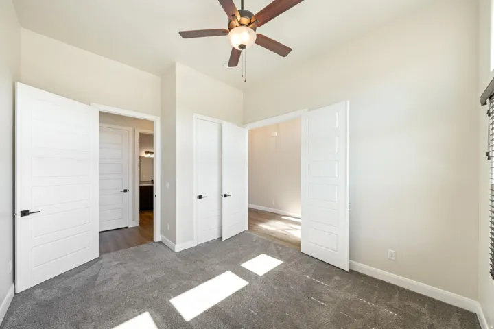 Carpeted room featuring a ceiling fan with integrated lighting, white panel doors with matte black hardware, and light-toned wall paint