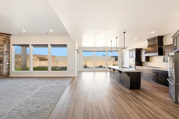 Open-concept living space featuring wood-finish flooring, a contemporary kitchen, stainless steel appliances, and a stacked stone fireplace