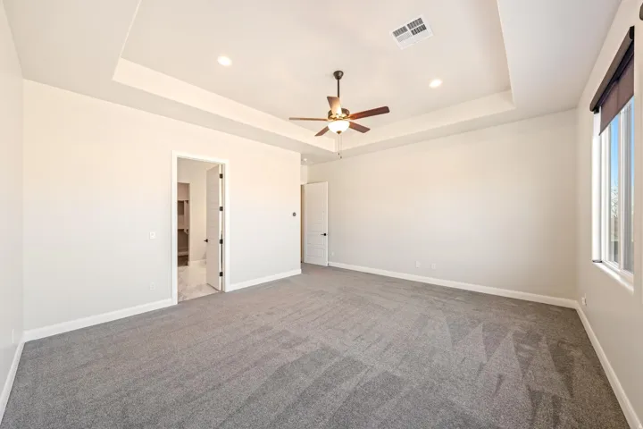 Spacious room featuring tray ceilings with recessed lighting, a ceiling fan, and grey carpet flooring