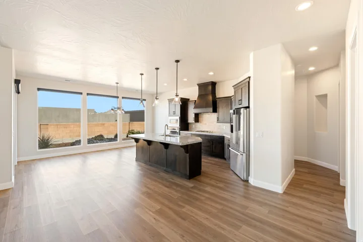 Open-concept living area with wood-finish flooring, a large kitchen island with pendant lighting, dark wood cabinetry, and stainless steel appliances