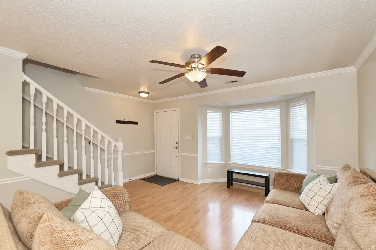 Living area featuring wood-finish flooring, a bay window with blinds, and a ceiling fan with light fixture