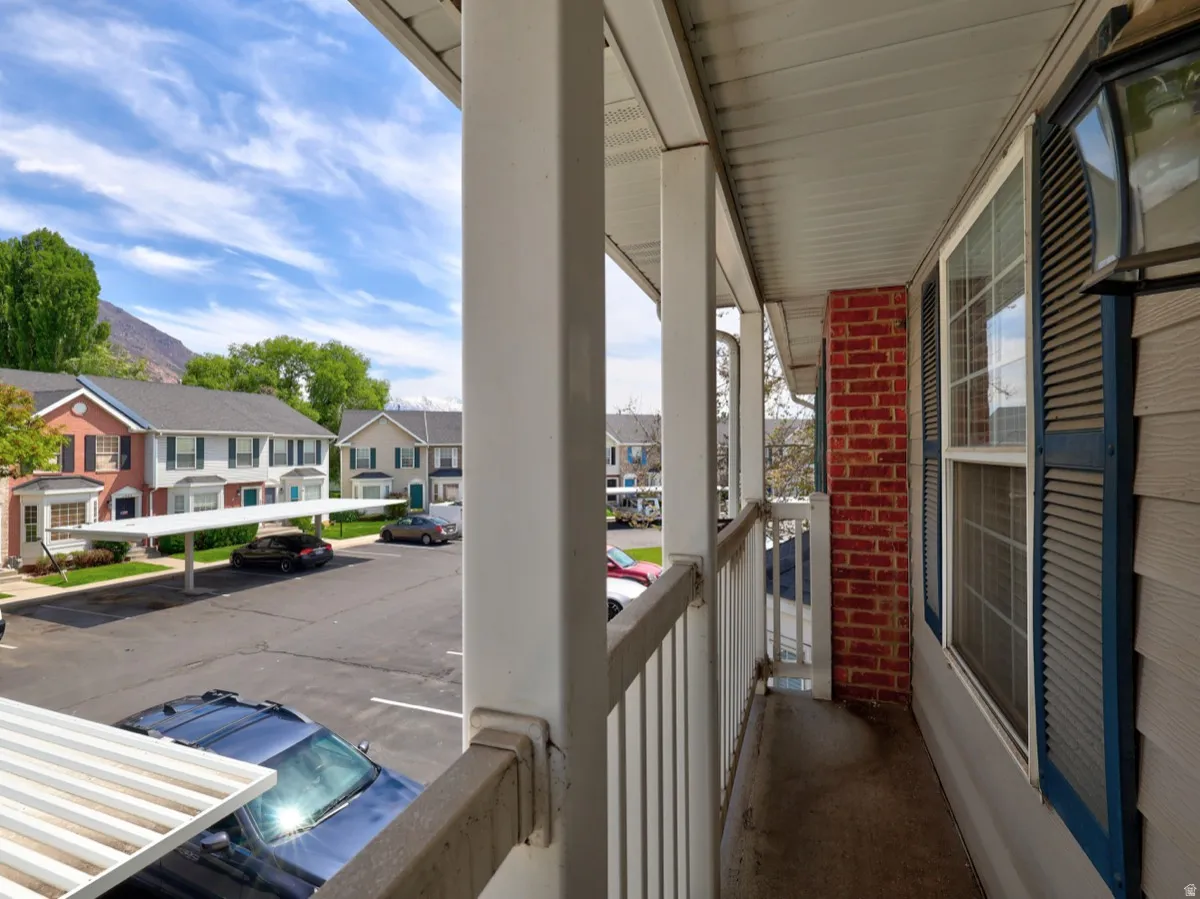 Covered exterior balcony featuring a brick accent wall, white railings, and a window with blue louvered shutters