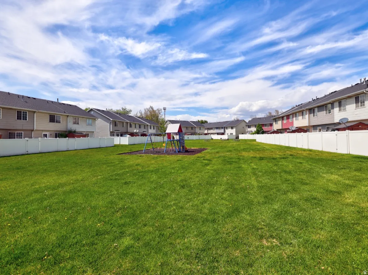 Expansive green space featuring a play structure with swings and a slide, surrounded by a white privacy fence