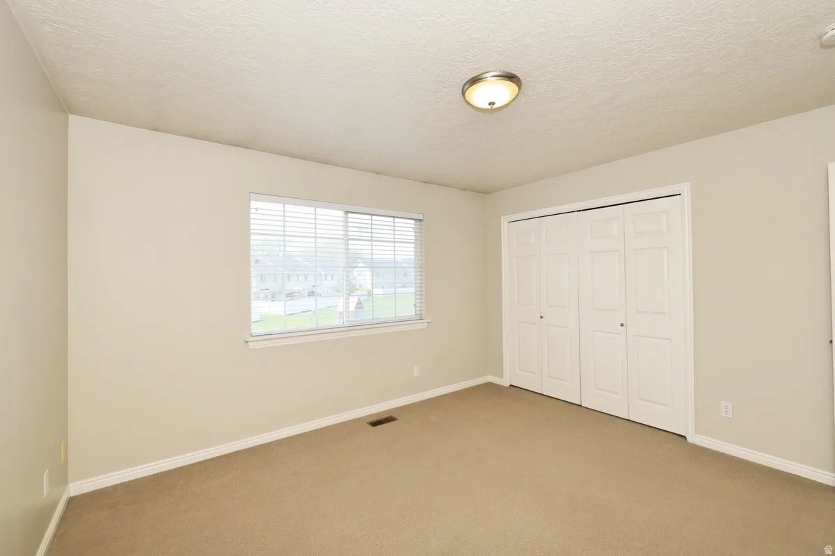 Neutral-toned room featuring a window with blinds, bi-fold closet doors, wall-to-wall carpeting, a flush-mount ceiling light fixture, and white baseboards