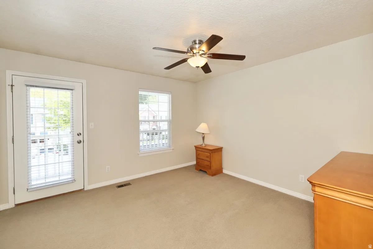 Spacious room featuring neutral carpeting, light-toned walls, and a ceiling fan with integrated lighting