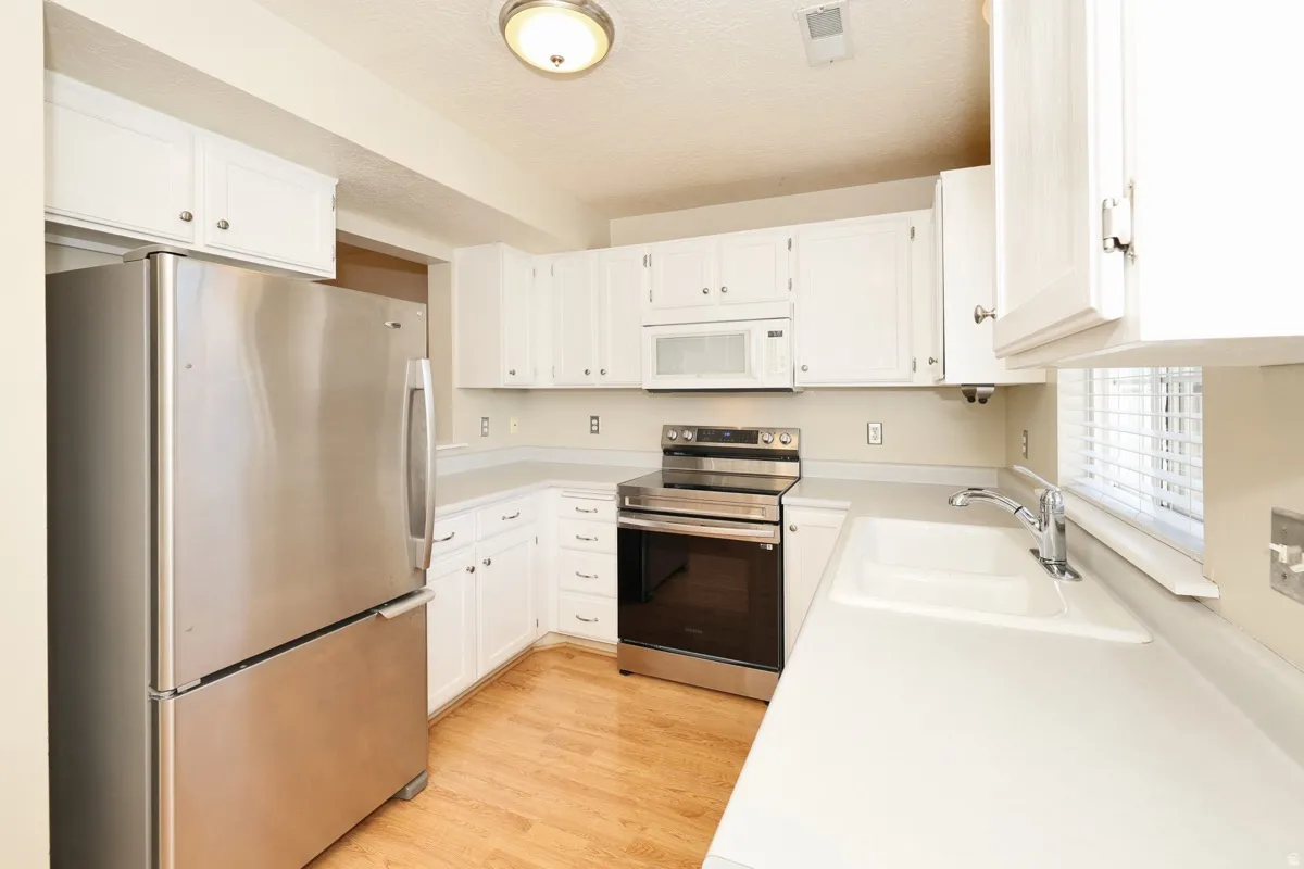 Kitchen featuring white cabinetry, light-toned countertops, stainless steel appliances, and wood-finish flooring