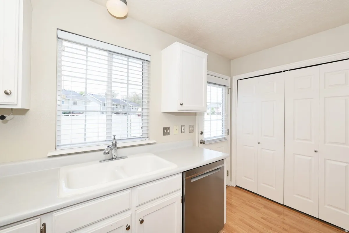 Kitchen area featuring white cabinetry, a double basin sink, a stainless steel dishwasher, and wood-finish flooring