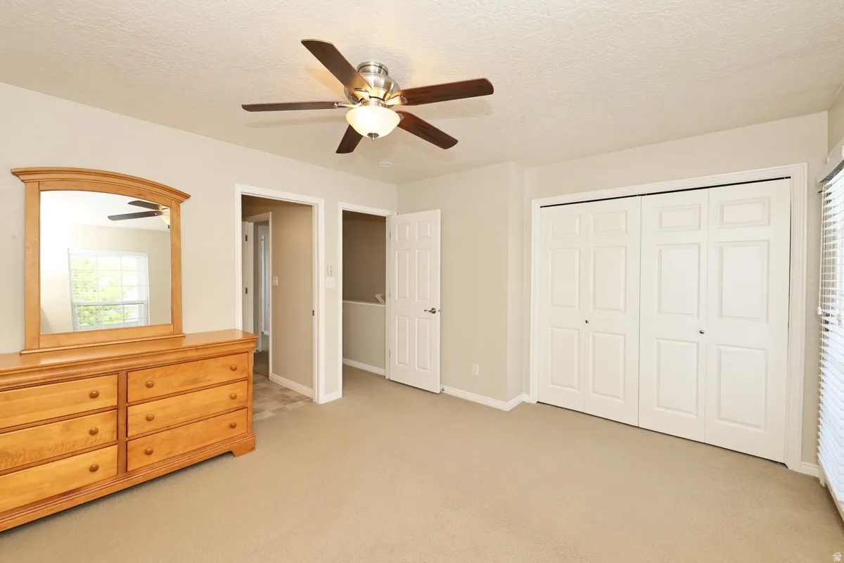 Carpeted room featuring a ceiling fan with integrated lighting, window with blinds, and white bi-fold closet doors
