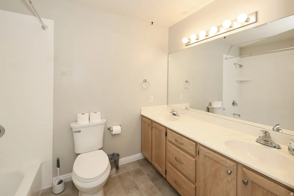 Bathroom featuring a dual vanity with light-tone cabinetry, a large integrated mirror, and a full bathtub with white tile surround