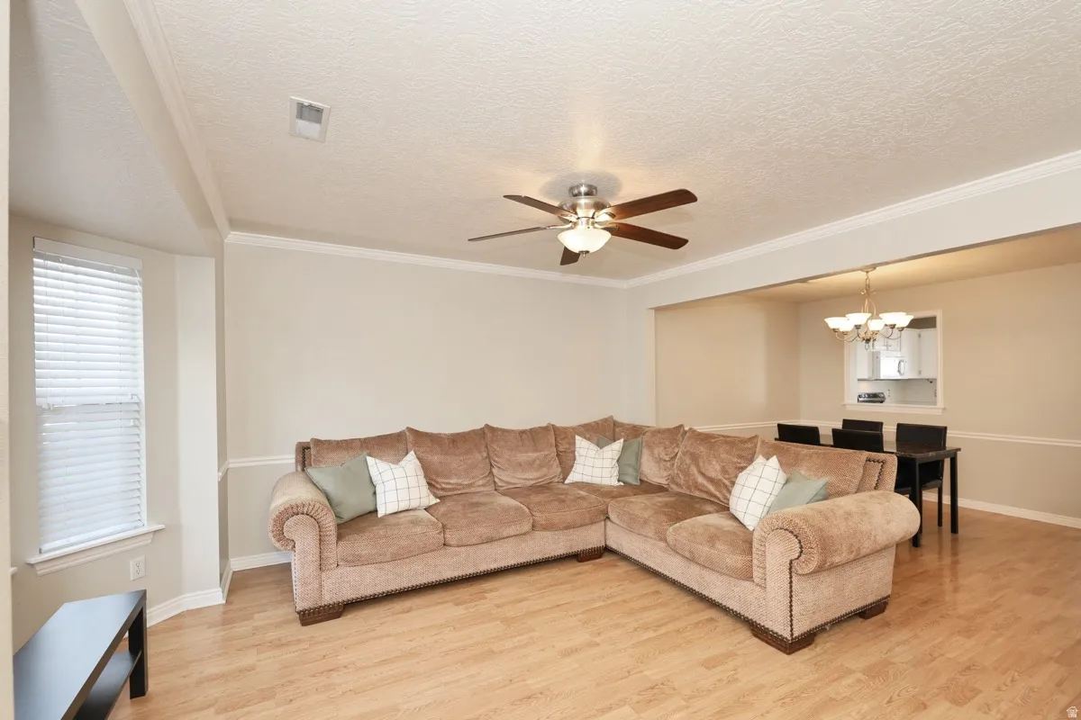 Open-concept living area featuring wood-finish flooring, a ceiling fan with light fixture, and a bay window with blinds