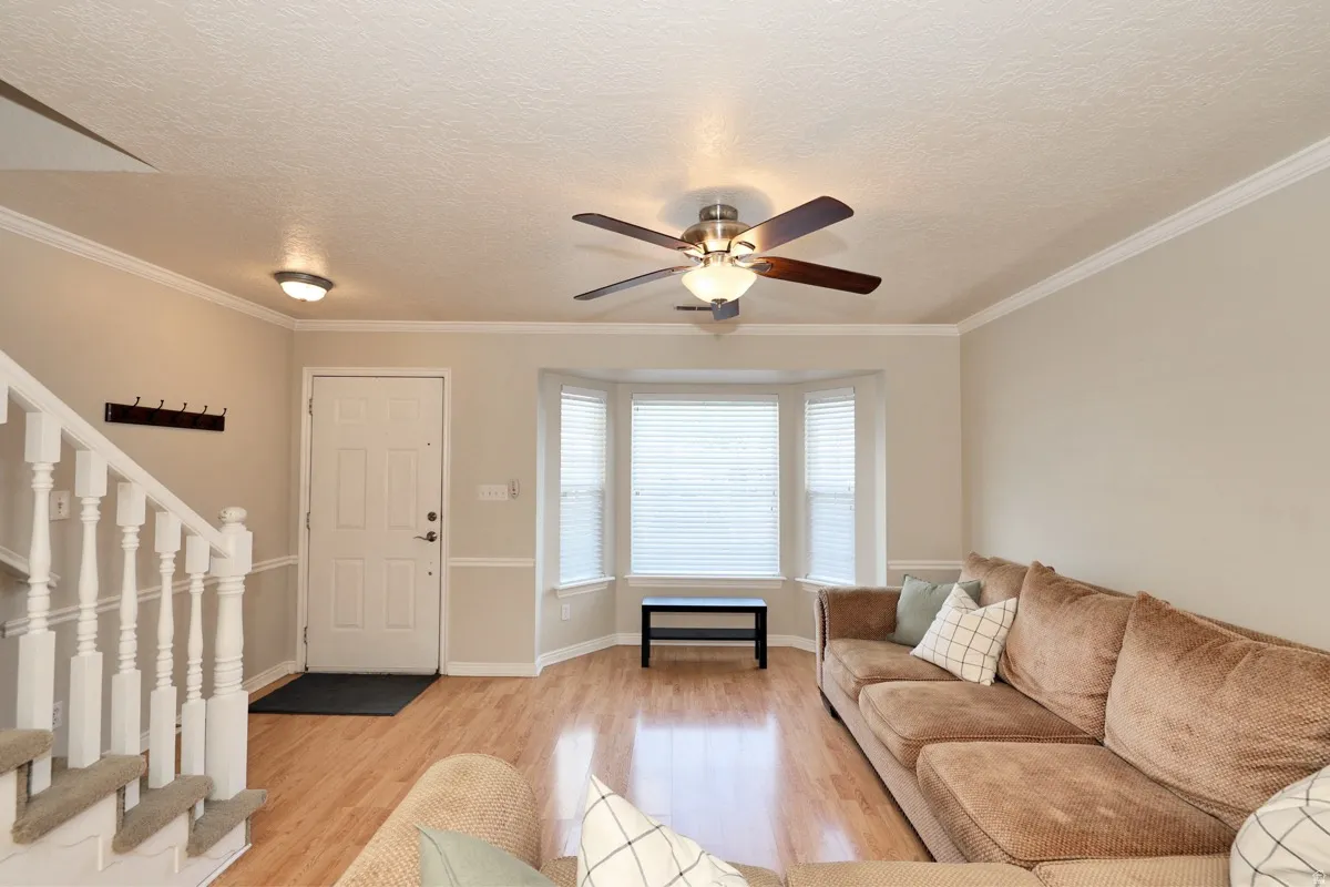 Bright living area featuring wood-finish flooring, a bay window with blinds, and crown molding